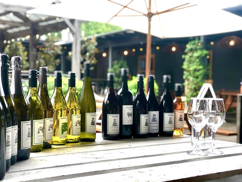 Row of wine bottles on a table outdoors with glasses.